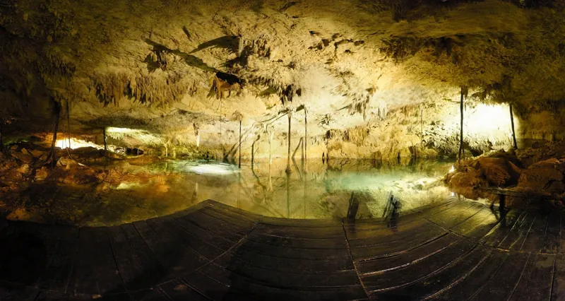 Panoramic view inside Cenote Taak Bi Ha: stalactites, roots and clear turquoise water seen from the wooden platform